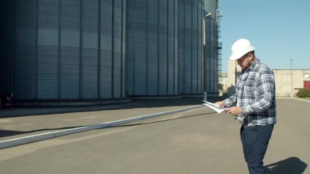 Professional engineer with blueprints inspecting agricultural silos — Stock Video