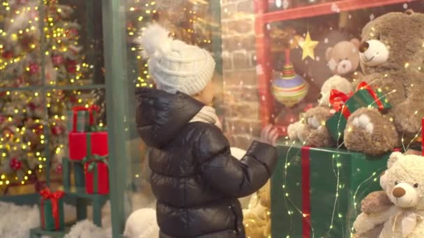Цікава дитина вивчає іграшки у вітрині магазину — стокове відео