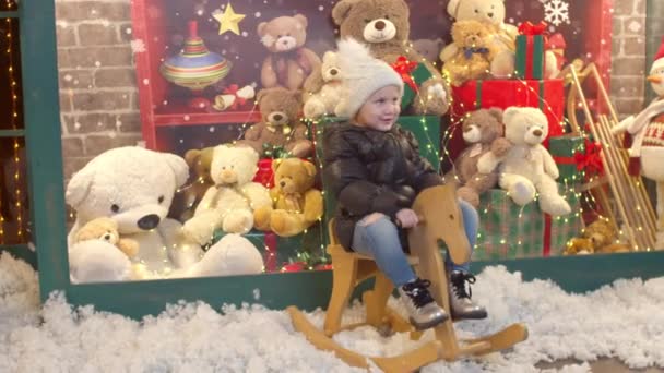 Niño feliz montar a caballo mecedora cerca de la tienda de juguetes — Vídeo de stock