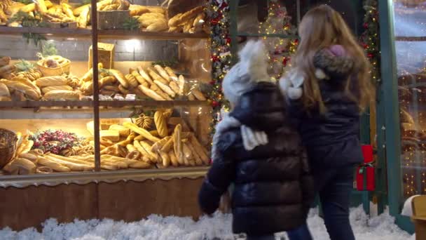 Chicas examinando el pan en la ventana de la panadería el día de Navidad — Vídeos de Stock