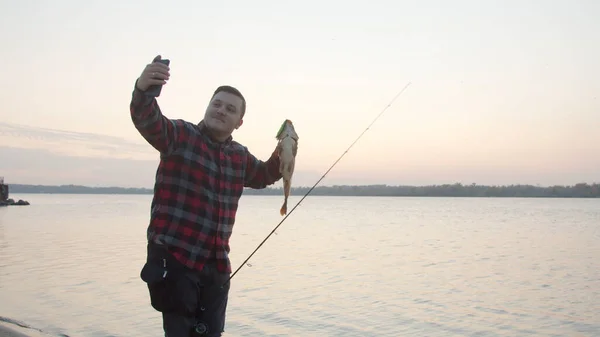 Muž rybář při selfie s rybami u vody — Stock fotografie