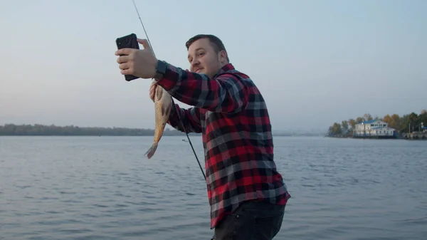 Pescador masculino tomando selfie con peces cerca del agua — Foto de Stock