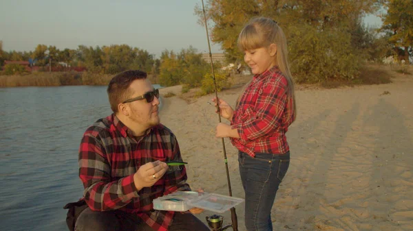 Padre mostrando cebo pescado a hija cerca del lago — Foto de Stock