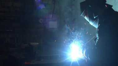 Karanlık atölyede metal kaynak yapan tanınmayan bir çalışan.
