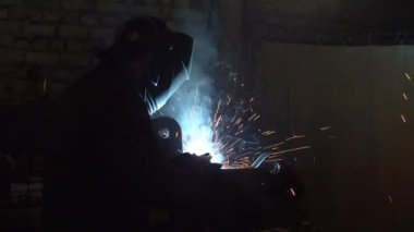 Karanlık atölyede metal kaynak yapan tanınmayan bir çalışan.