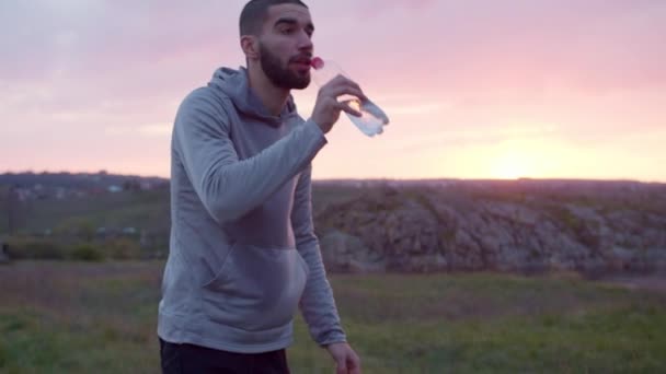 Utmattad idrottsman dricksvatten efter träning i fält — Stockvideo