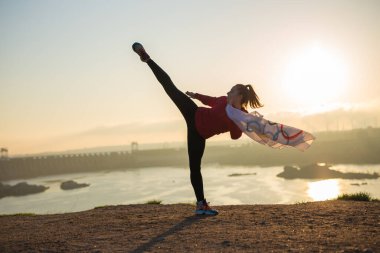 Bayrak taşıyan kadın gün batımında dövüş sanatları egzersizi yapıyor.