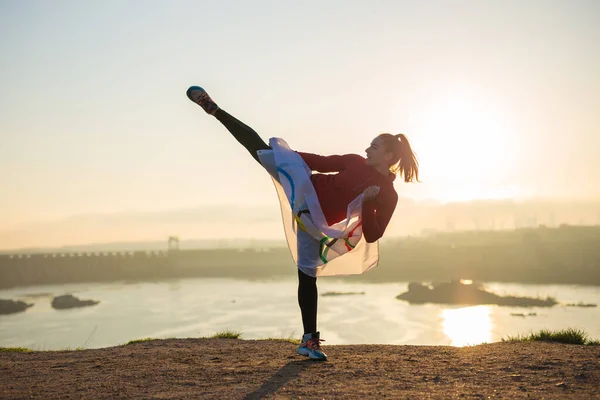 Woman with flag doing martial arts exercises at sunset light