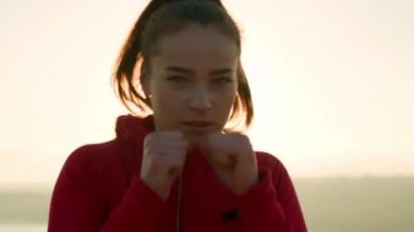 Kendine güvenen genç sporcu kadın gün batımında yumruk talimi yapıyor.