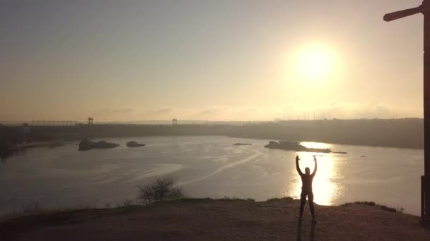 Жінка практикує бойові мистецтва на березі річки на заході сонця — стокове відео