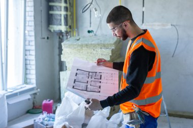 Tamir odasından önce elinde kağıt bir daire planı tutan bir erkek işçi. 