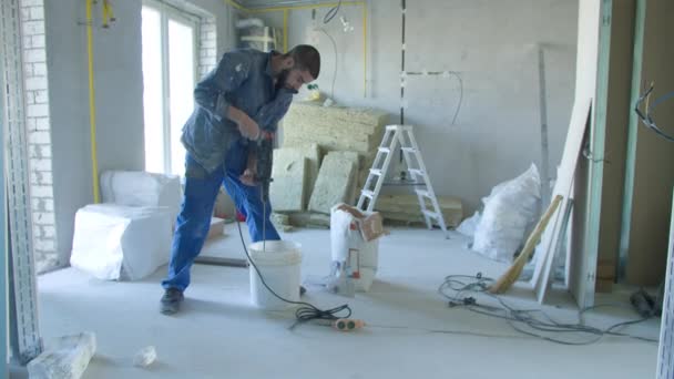 Mannelijke bouwer mengen stucwerk met boor in emmer — Stockvideo