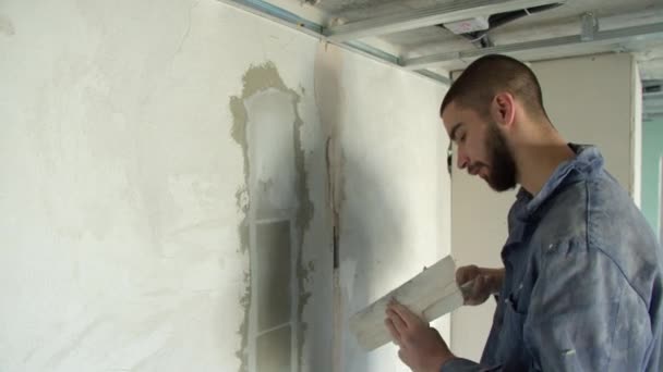 Дружественный мужчина-строитель разбрасывает штукатурку по стене — стоковое видео