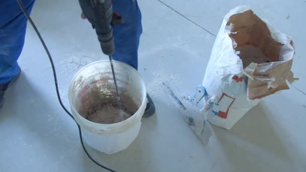 Мужчина-строитель смешивает штукатурку с дрелью в ведре — стоковое видео