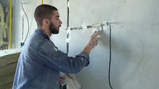 Bearded contractor spreading plaster on wire trunking — Stock Video