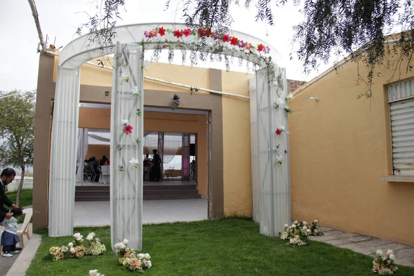 Arco blanco con decacion de flores y Plantas colgantes al aire libre, colocado a la entrada del local donde se desarrolar la recepcion de matrimonio. Imagen ideal para promocionar dekaraciones de eventos.