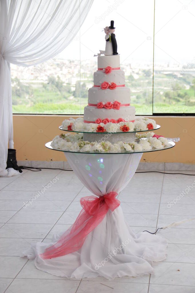 Pastel de Bodas de color blanco con decoracion de flores comestibles, todo sobre una mesa de cristal; en la parte de arriba se tiene la representacion de los recien casados. Imagen ideal para promocionar pasteleria.