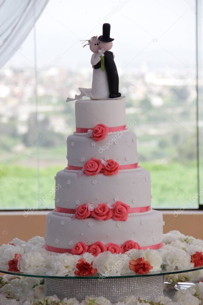 Torta de matrimonio de color blanco con decoracion de flores comestibles, en la parte de arriba se puede ver la representacion de los recien casados. Imagen ideal para promocionar pasteleria.