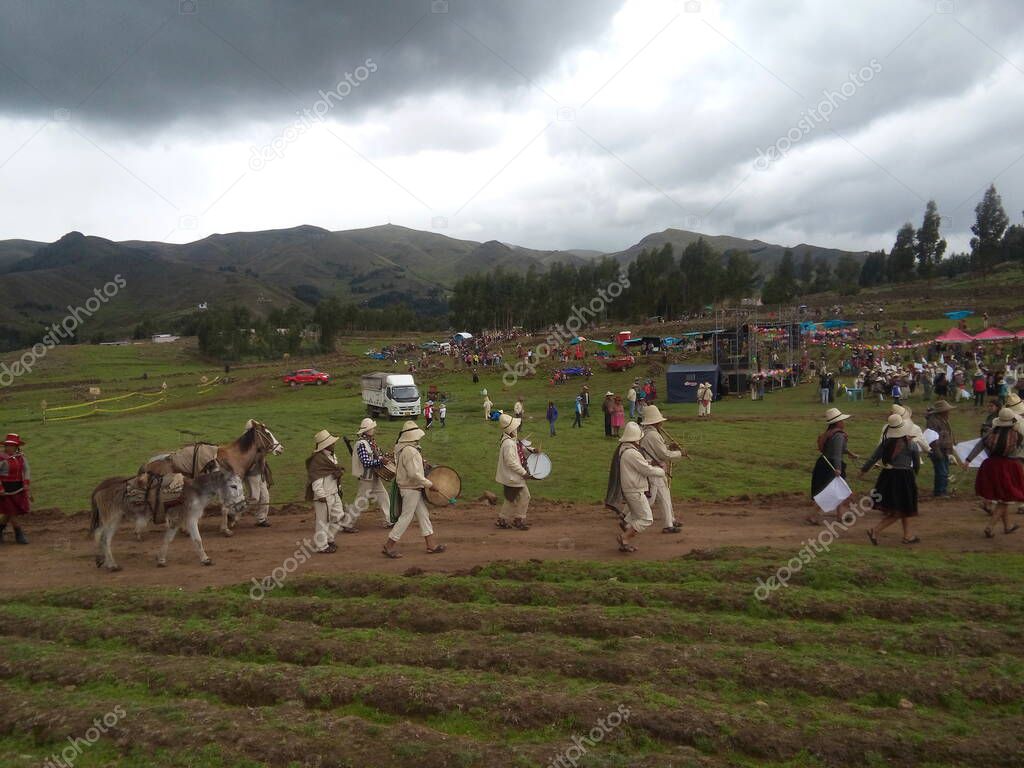 Pasacalles con danzas, musicos y animales oriundos en la sierra del Peru, por fiesta patronal, a lo lejos se observa en contraste de los cerros con el cielo a punto de nublarse