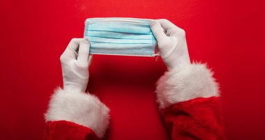 Noel Baba ellerinde koronavirüs cerrahi yüz maskesi tutuyor. Kapalı Noel