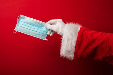 Noel Baba ellerinde koronavirüs cerrahi yüz maskesi tutuyor. Kapalı Noel