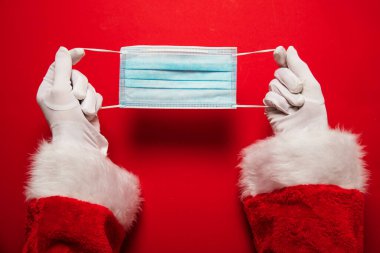 Noel Baba ellerinde koronavirüs cerrahi yüz maskesi tutuyor. Kapalı Noel