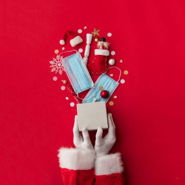 Noel Baba koruyucu maskelerle patlayan bir Noel hediyesi tutuyor.