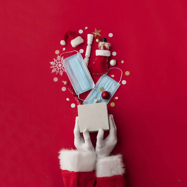 Papai Noel segurando um presente de Natal explodindo com máscaras protetoras — Fotografia de Stock