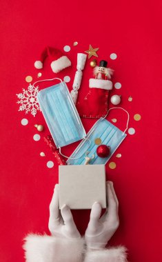 Noel Baba koruyucu maskelerle patlayan bir Noel hediyesi tutuyor.