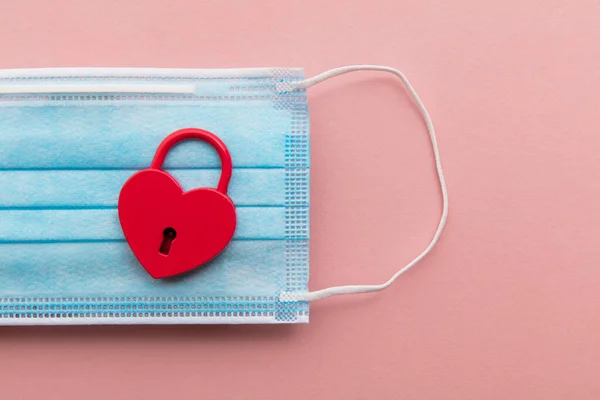 Amor en Lockdown. Candado de San Valentín en forma de corazón rojo sobre una máscara de coronavirus — Foto de Stock