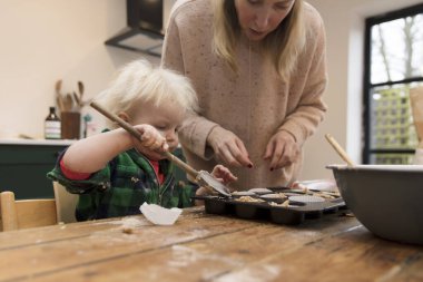 Mutlu küçük çocuk ve anne mutfakta kek pişiriyor. .