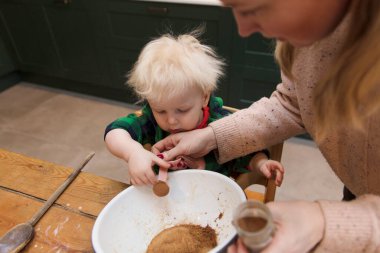 Genç bir çocuk, annesine mutfaktaki karıştırma kabına malzeme eklemesi için yardım ediyor..