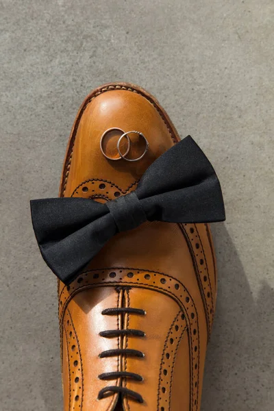 Бабочка и обручальные кольца на коричневой кожаной обуви жениха — стоковое фото