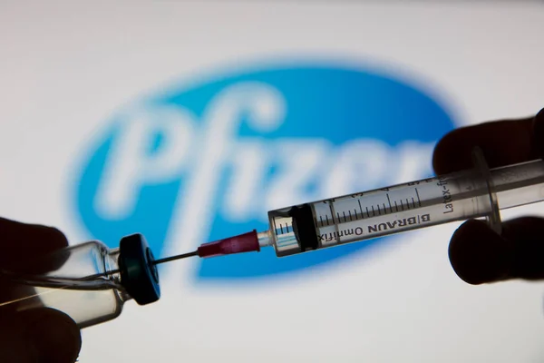 OXFORD, İngiltere - Şubat 2020: Pfizer logosu önünde bir covid aşı şırıngası — Stok fotoğraf