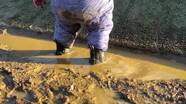 Uma criança a saltar e a brincar numa poça lamacenta. Movimento lento — Vídeo de Stock