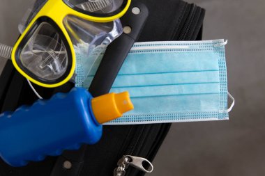 Coronavirus seyahat eder. Yüz maskeli güneş kremi ve dalgıç maskeli çanta.