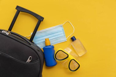 Covid yaz tatili. Yüz maskeli güneş kremi ve dalgıç maskeli bir valiz.