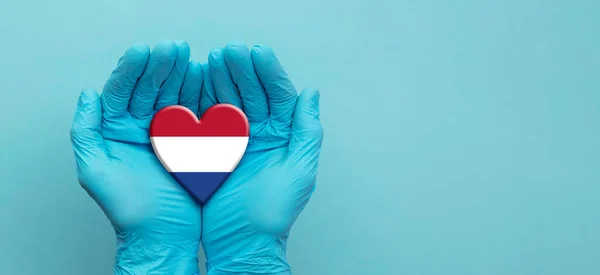 Artsen handen dragen chirurgische handschoenen met Nederlandse vlag hart — Stockfoto