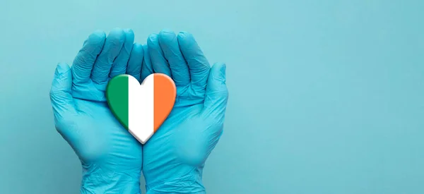 Médicos con las manos con guantes quirúrgicos sosteniendo la bandera de Irlanda corazón — Foto de Stock