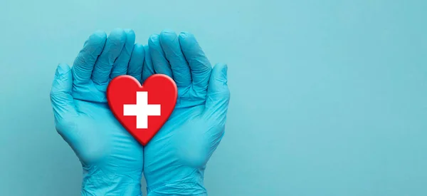 Médicos con guantes quirúrgicos sosteniendo el corazón de la bandera de Suiza — Foto de Stock