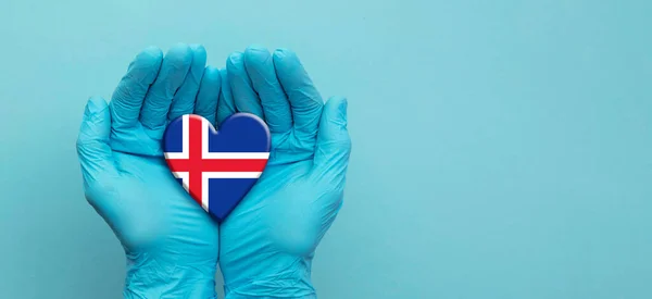 Orvosok kéz visel sebészeti kesztyű tartja Izland zászló szív — Stock Fotó