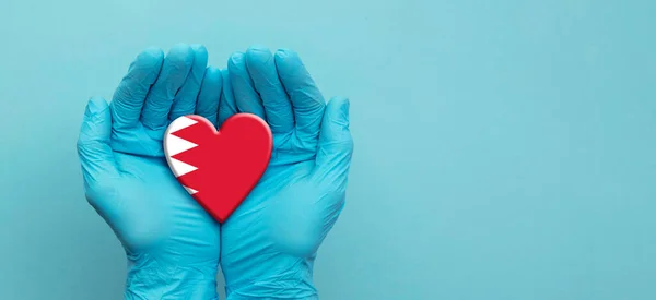 Médicos usando guantes quirúrgicos sosteniendo la bandera de Bahréin corazón — Foto de Stock