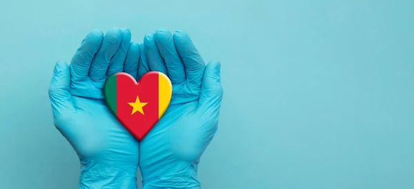 Medici mani che indossano guanti chirurgici tenendo il cuore bandiera Camerun — Foto Stock