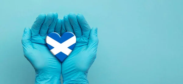Médicos con guantes quirúrgicos sosteniendo el corazón de la bandera de Escocia — Foto de Stock
