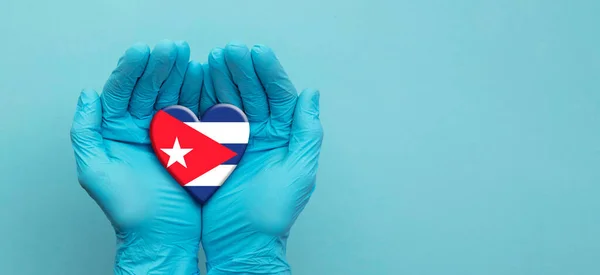 Médecins mains portant des gants chirurgicaux tenant Cuba drapeau coeur — Photo