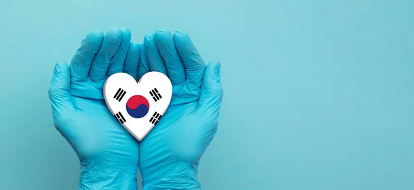 Orvosok kéz visel sebészeti kesztyű tartja Dél-Korea zászló szív — Stock Fotó