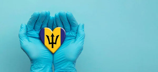 Lékařské ruce v chirurgických rukavicích držící vlajkové srdce Barbadosu — Stock fotografie