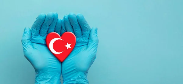Médicos mãos vestindo luvas cirúrgicas segurando coração bandeira Turquia — Fotografia de Stock