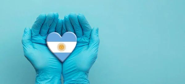 Läkare händer bär kirurgiska handskar håller Argentina flagga hjärta — Stockfoto