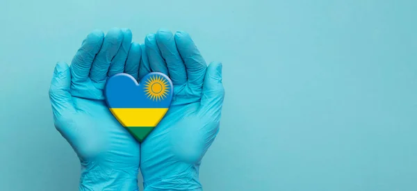 Mains de médecins portant des gants chirurgicaux tenant le drapeau du Rwanda coeur — Photo
